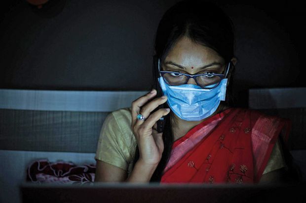 Young Indian Woman wearing mask working on her laptop and talking on phone