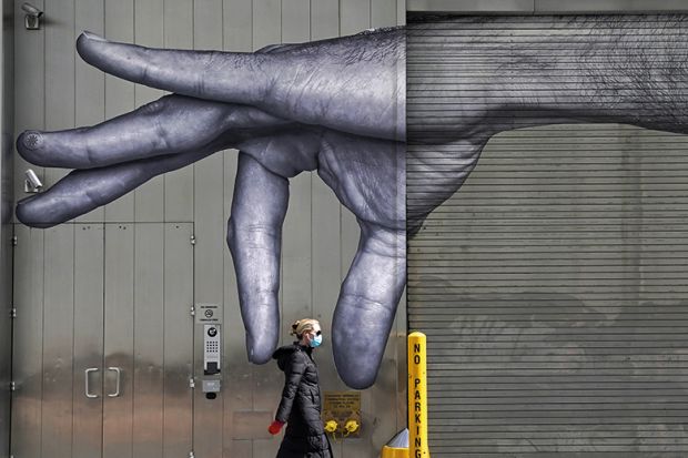 A woman in a mask walks past a mural of a hand on the side of a building in Midtown New York City  April 22, 2020
