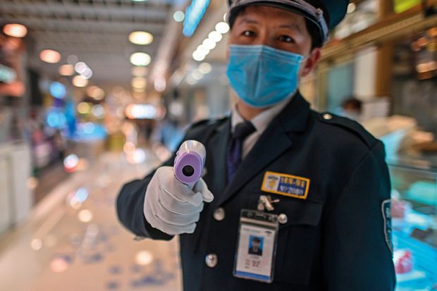 A guard wearing a facemask amid concerns over the spread of the COVID-19 novel coronavirus, holds a thermal gun to check the body temperature of visitors at the entrance of a restaurant area in Shanghai, on March 21, 2020.