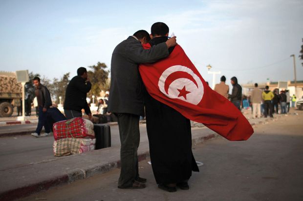 Two men, one wearing the flag of Tunisia, stand at the border of Libya on February 28, 2011 in Ras Jdir, Tunisia