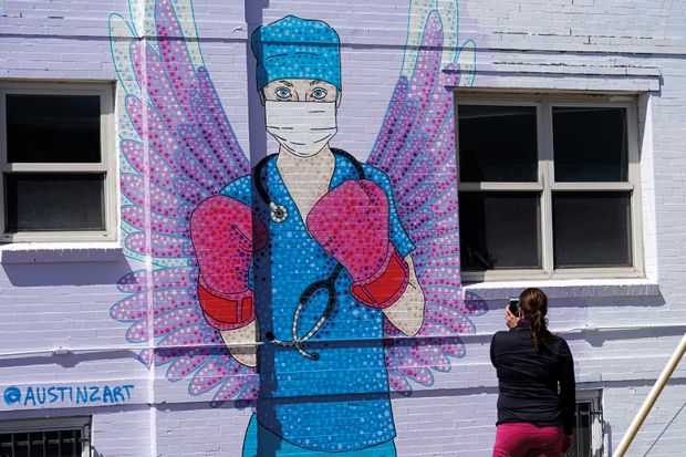A woman shoots a picture of a mural depicting a medical worker with a mask covering her mouth and nose, wearing boxing gloves and angel-like wings on her back is seen on April 14, 2020 in downtown Denver, United States