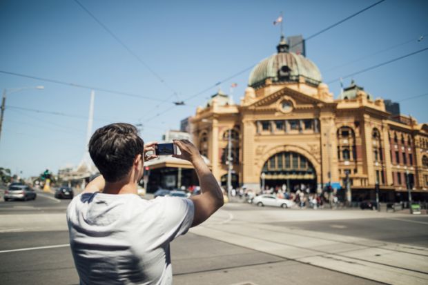  tourist is using his smart phone to take a photo of Flinders Street Train Station in Melbourne, Victoria