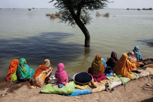 A group of women watch the floodwaters slowly rise to illustrate West’s ‘self-imposed boundaries’ hinder Pakistan