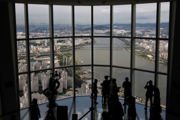 Visitors are silhouetted as they take photographs at the glass-bottomed Seoul Sky observation deck to illustrate UK university explores options in South Korea’s forgotten hub