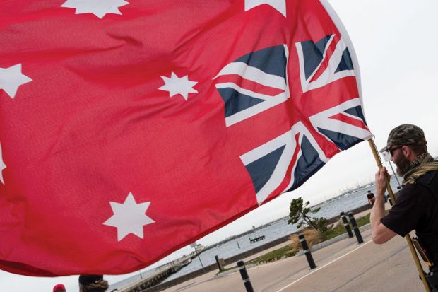 Person holding an upside down Red Ensign flag in Australia as a metaphor that legal academics say ‘Top-down’ rules won’t solve free speech fears.