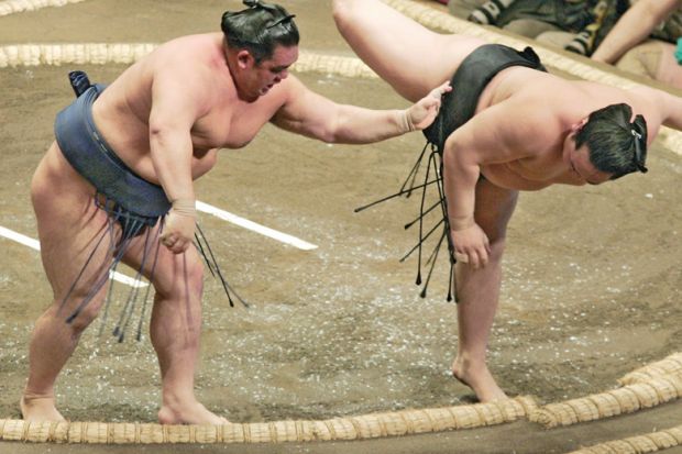 A sumo grand champion is forced down the ring by balancing on the edge of it to illustrate Universities struggle to live up to Japan’s research ambitions