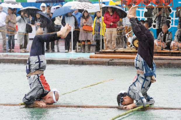 Two performers stand on their heads on a floating square lumbers at a local festival in Tokyo to illustrate academics ‘reluctant’ to recommend Japan as borders stay shut