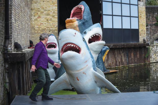 Person in front of a display of a group of full-scale replica sharks as a metaphor for Predatory journals jeopardise PhDs