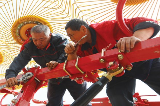 Equipment technicians repair a wheel rake in a field in China as a metaphor for overseas students fear losing degrees as China borders stay shut