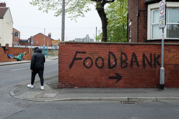 Person passes by bold, black graffiti that points towards a local food bank to illustrate that One in four UK universities now running a food bank