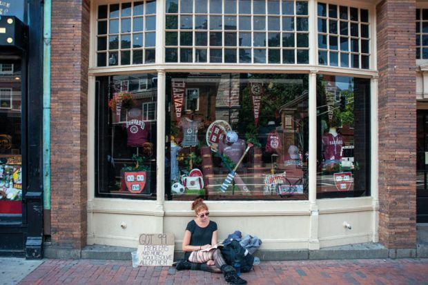 Young homeless girl sitting outside the Harvard University T-shirts books and souvenirs store in the city center Massachusetts Avenue, Cambridge, Massachusetts, USA to illustrate edX architects tackle online access afresh with Axim 