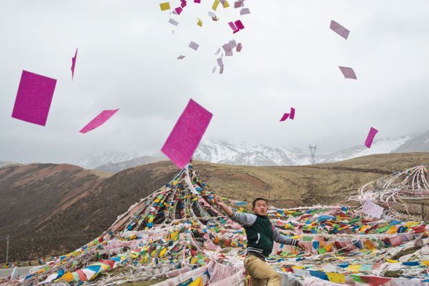 A Tibetan man throws prayers in the air at a high altitude as a metaphor for leading Chinese universities axe publication condition for PhDs