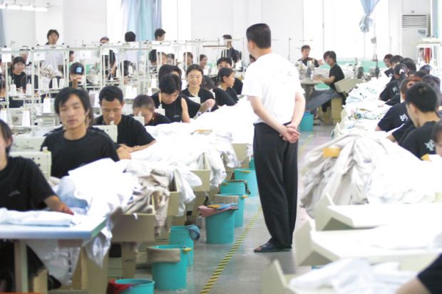 China, sweatshop manager standing watching workers