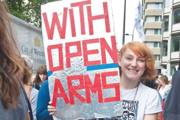 Person in a refugee demonstration London UK holding a banner reading 'With Open Arms'