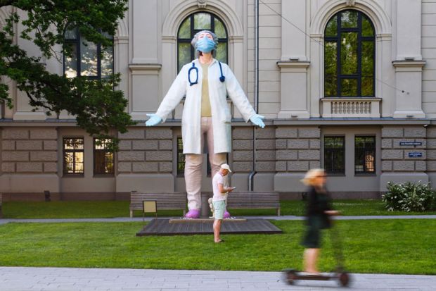 A woman on a scooter drives past a 6 meters high statue of a female doctor by Latvian artist Aigars Bikse called "Medics to the World" as a metaphor for ‘Dramatic’ variation in universities’ occupational health expenditure