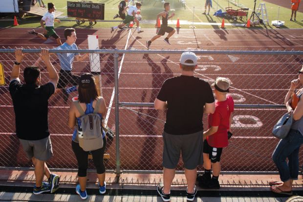 People watch from behind the fence as the athletes cross the finish line as a metaphor for the wealth gap widening as US elite report record enrolments