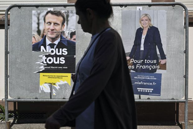 A pedestrian walks past campaign posters of French President and La Republique en Marche (LREM) party candidate for re-election Emmanuel Macron (L) and French far-right party Rassemblement National (RN) presidential candidate Marine Le Pen in Mulhouse