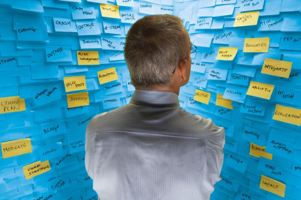 Middle-aged man standing in front of wall covered in sticky notes to illustrate Big HE ideas are plentiful. Why aren’t v-cs listening?