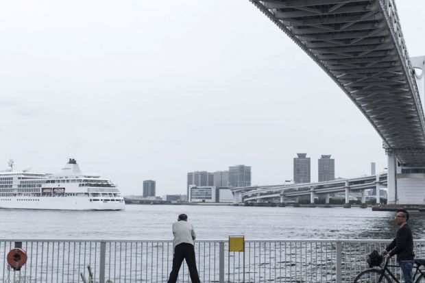 A man observes a ship passing under the Rainbow Bridge in Tokyo, Japan as a metaphor for Japan ‘will  miss the boat’  if it doesn’t  go global
