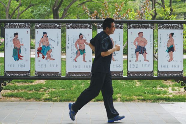 A man runs past a billboard showing Chinese medicine at a park in Beijing as a metaphor for Hong Kong to give Chinese medicine thorough check-up 