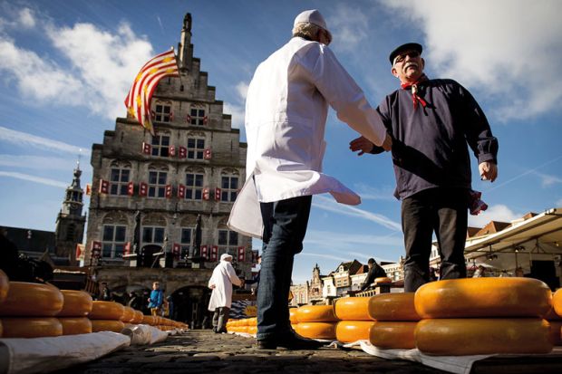 Shaking hands with a Cheesemaker at a market at the opening of the Dutch Cheese season in Goudato illustrate UK universities near Elsevier deal after publisher drops price