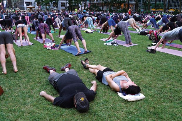 A couple of tourists nap in the grass as people participate in an outdoor yoga event to illustrate US universities mull adopting New York college’s four-day week