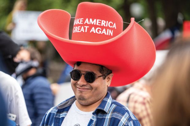 A person wears an oversized "Make America Great Again" hat as a metaphor for the US lawmakers to adopt philanthropic tactics for dictating academic content