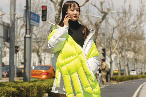 Lady wearing wearing neon quilted large hand design in Shanghai, China as a metaphor for a rigid system pushes Chinese students to use private agents.