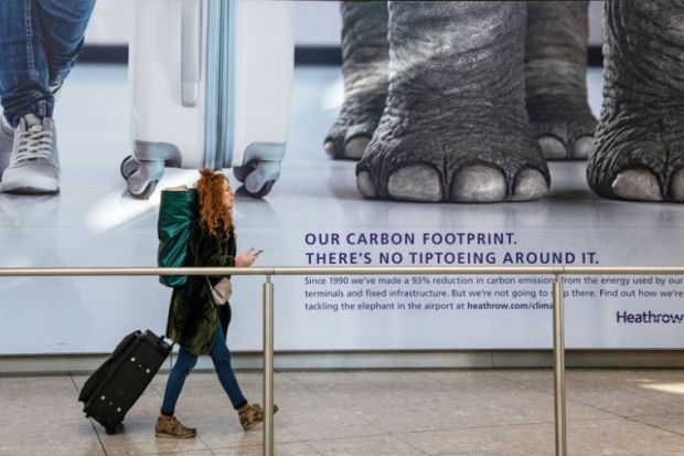 Air passengers walk past a poster advertising Heathrow's commitment to reducing carbon emission as a metaphor for Green-minded universities fail to set net zero targets