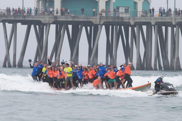Crowds gather on the pier and the beach to watch surfing break the World Guinness Record for most people (66) on a surfboard and the biggest surf board (42 1/4 feet) in Huntington Beach, California to illustrate Biden officials open to more three-year deg