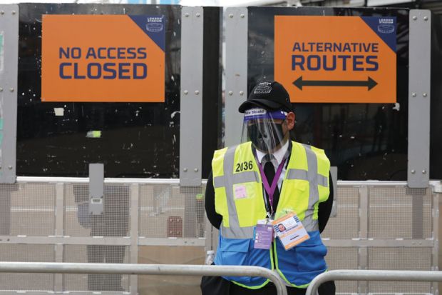 A steward in PPE including face mask and visor as a precaution against COVID-19 staffs a barrier at The London Stadium