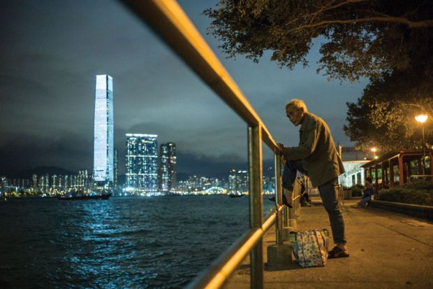 An elderly man rests his foot on a railing as he fishes in the waters of Victoria Harbour in Hong Kong