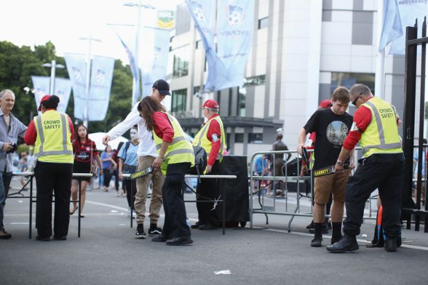 Crowd safety personnel inspecting bags of attendees outside a sports stadium