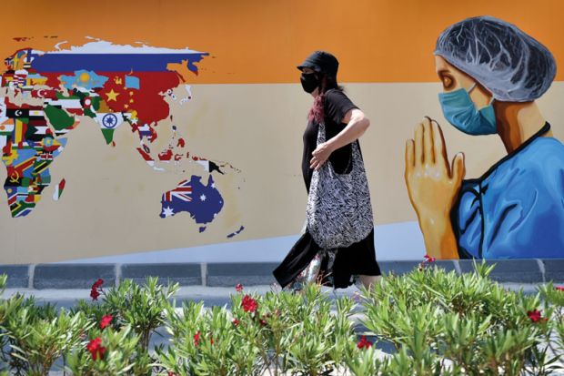 A woman wearing face mask walks past a mural depicting of a healthcare worker and a world map with flags on walls 