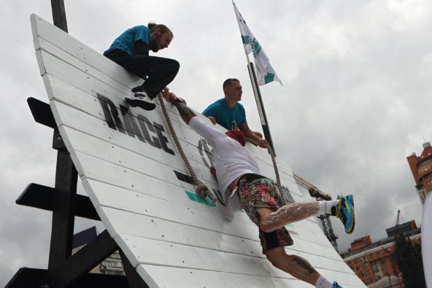 An athlete lends a helping hand to another contestant climbing up the warped wall 