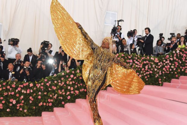  on the red carpet person wearing  huge gold sparkle angel wings