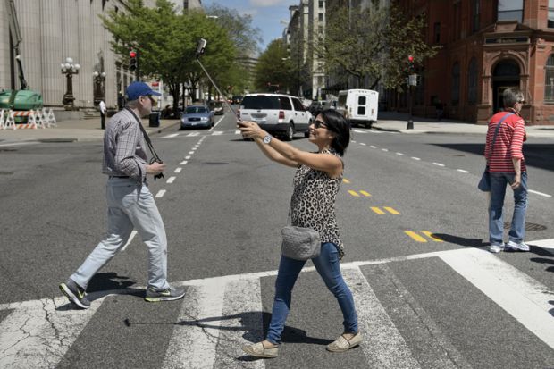 Woman using smartphone selfie stick while crossing road