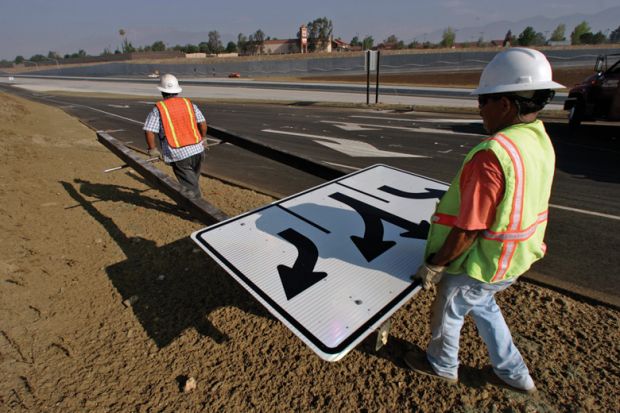 Workmen carrying traffic sign along roadside