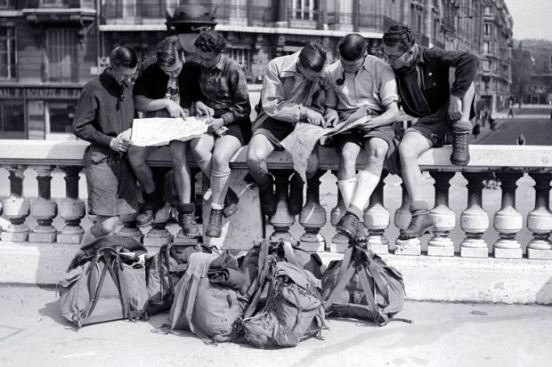 Young men sitting on a wall looking at maps