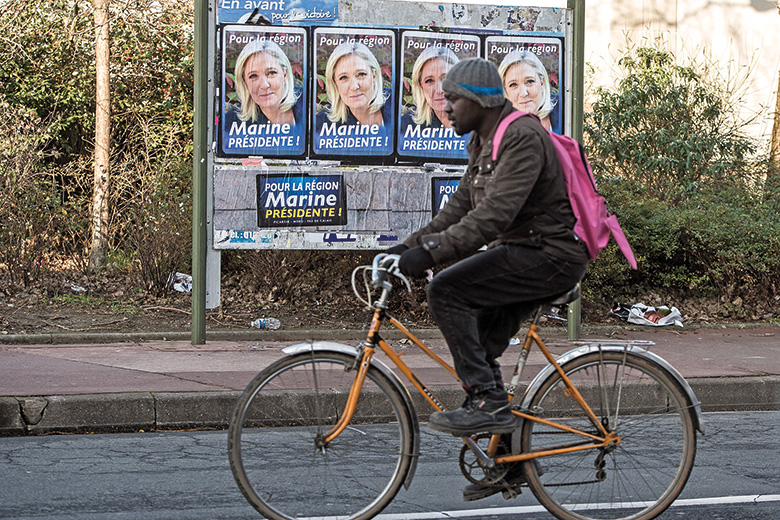 A cyclist going past a series of Marine Le Pen posters